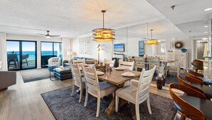 A spacious living area with a dining table, chairs, and a large window overlooking the sea. - SD 410: Seaside Summit - Watch the Sun Sink into the Gorgeous Gulf! (Fort Walton Beach)