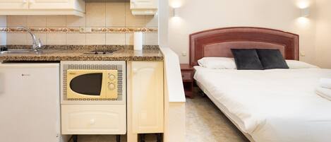Una habitación de hotel compacta con kitchenette, una cama con ropa de cama blanca y un cabecero de madera.