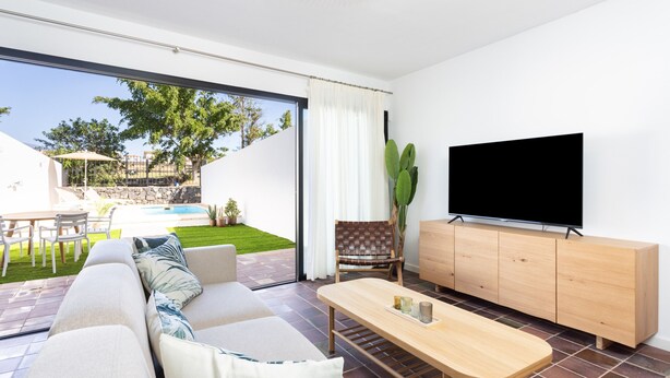 A modern living room with a sofa, coffee table, TV, and a sliding glass door leading to a pool area. - Marvelous home with private pool (San Miguel de Abona)