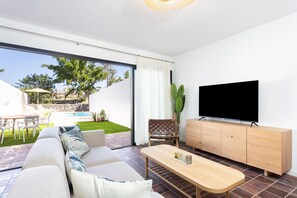 A modern living room with a sofa, coffee table, TV, and a sliding glass door leading to a pool area.