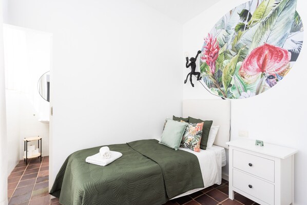 A bedroom with a bed, a nightstand, a wall-mounted mirror, and a floral mural.