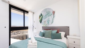 A bedroom with a bed, a nightstand, a wall art piece, and a view of a rocky landscape through a window. - Marvelous home with private pool (San Miguel de Abona)