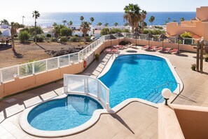 A swimming pool with a view of the sea, surrounded by lounge chairs and palm trees. - Nice apt with terrace in Golf del Sur (San Miguel de Abona)