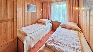 Una cabaña con dos camas individuales, paredes de madera, una ventana con cortinas y un pequeño cuadro en la pared.