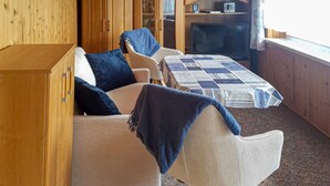 Una habitación acogedora con sofá, sillón, mesita y cama con colcha a cuadros.