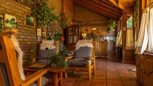 A cozy, rustic interior with wooden furniture, a brick wall adorned with framed photos, and a tiled floor.