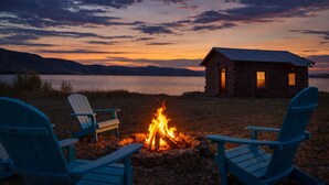 A cabin by a lake at dusk with a fire in front and two Adirondack chairs. - Henry`s Lake View Cabin + BBQ + Fire Pit + Decks! (Island Park)