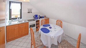 Eine kleine Küche mit Holzausbau, Fliesenboden in Weiß und einem Esstisch mit blauen Tischsets.