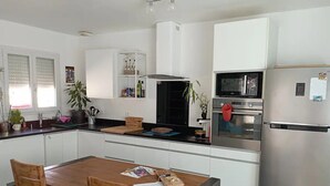 A modern kitchen with white cabinets, a stainless steel refrigerator, a microwave, and a stove. There is a wooden dining table with chairs. - Vacances à 10 Minutes des Plages, Avec BBQ et Piscine (Châteauneuf les Martigues)