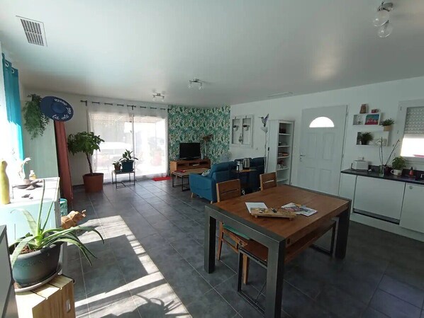 A spacious living room with a dining area, a kitchen, and a TV in the background.