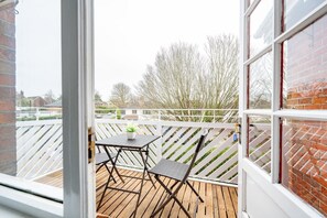 A wooden deck with a table and chairs, a white railing, and a view of trees and buildings.