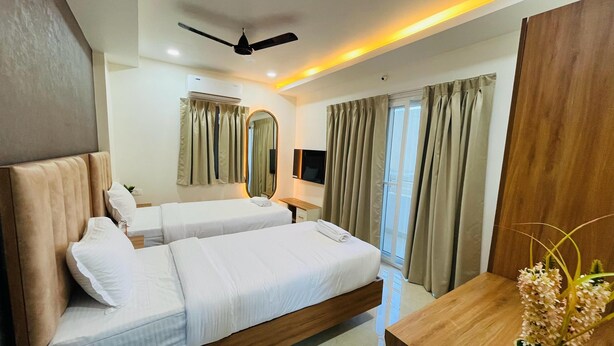 A hotel room with two beds, a ceiling fan, a flat-screen TV, a wooden desk, and a large mirror. - Viola Suites (Hyderabad)