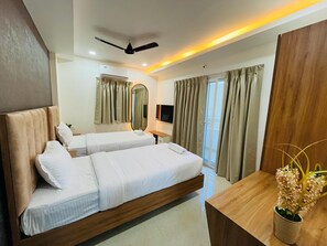 A hotel room with two beds, a ceiling fan, a flat-screen TV, a wooden desk, and a large mirror. - Viola Suites (Hyderabad)