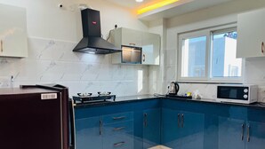 A modern kitchen with blue cabinets, a gas stove, a microwave, and a black range hood. - Viola Suites (Hyderabad)