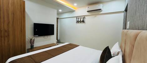 Une chambre d’hôtel équipée d’un lit, d’un ventilateur de plafond, d’un appareil de climatisation, d’un téléviseur à écran plat et d’une petite étagère ornée d’objets décoratifs.