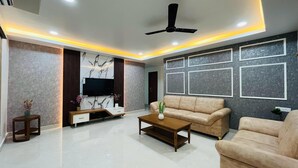 A modern living room with a flat-screen TV, beige sofas, a coffee table, and a ceiling fan. - Viola Suites (Hyderabad)