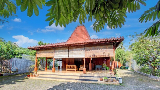 Een traditioneel houten huis met pannendak, een overdekte veranda en een met baksteen bestraate binnenplaats.