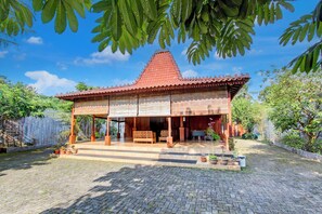 A traditional wooden house with a tiled roof, a covered porch, and a brick-paved courtyard.