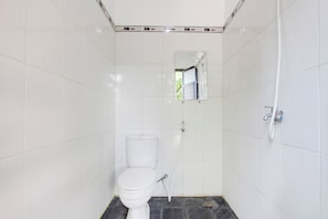 A small, tiled bathroom with a toilet, a shower, and a mirror.