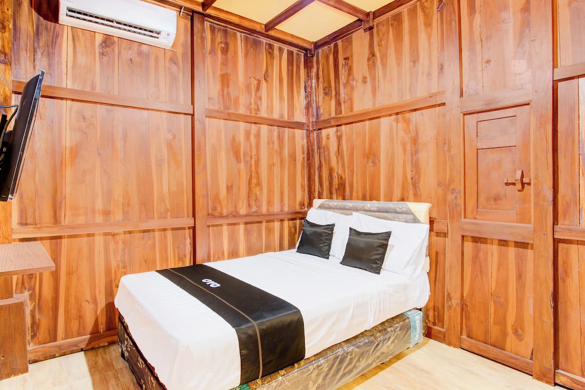 Een kamer met houten lambrisering, een bed, een flatscreen televisie aan de muur en een houten deur.