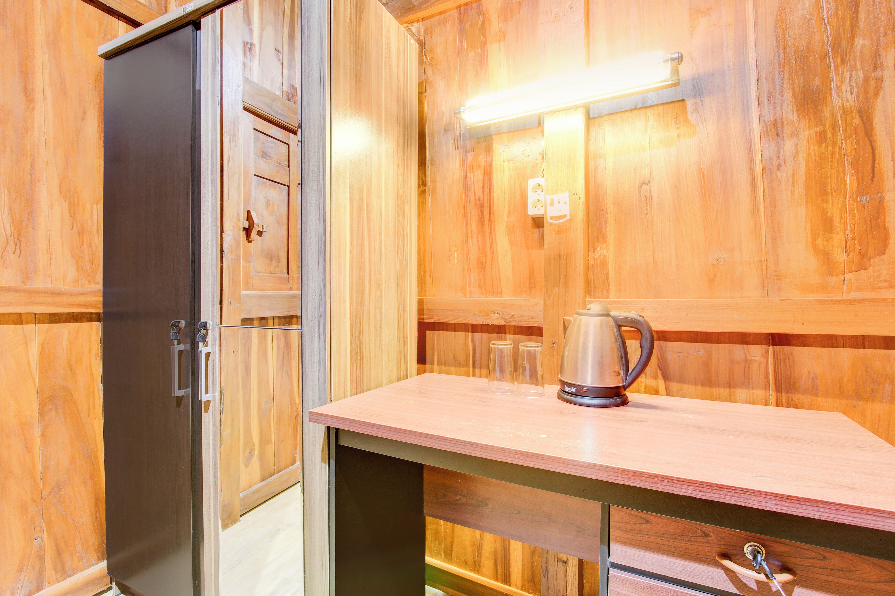 Interior em madeira com área de cozinha compacta, incluindo geladeira, bancada com chaleira e luminária fixada na parede.