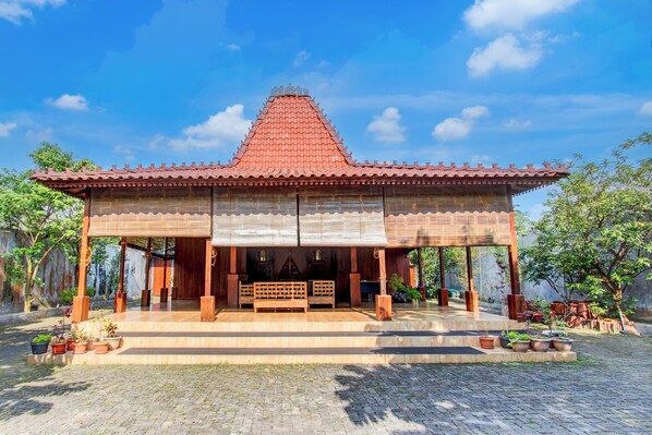A traditional wooden pavilion with a tiled roof, surrounded by potted plants and trees.