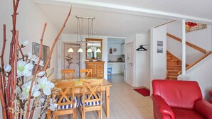 A dining area with a wooden table and chairs, a red leather sofa, and a staircase leading to another level. - Ferienhaus Ostseebad Breege (Ostseebad Breege)