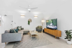 A modern living room with a grey sofa, a small coffee table, a TV on a wooden stand, and a ceiling fan.