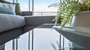 A modern living room with a sofa, a glass coffee table, and a potted fern. - Waterfront Apartment with Rooftop Pool and Views (Cairns City)