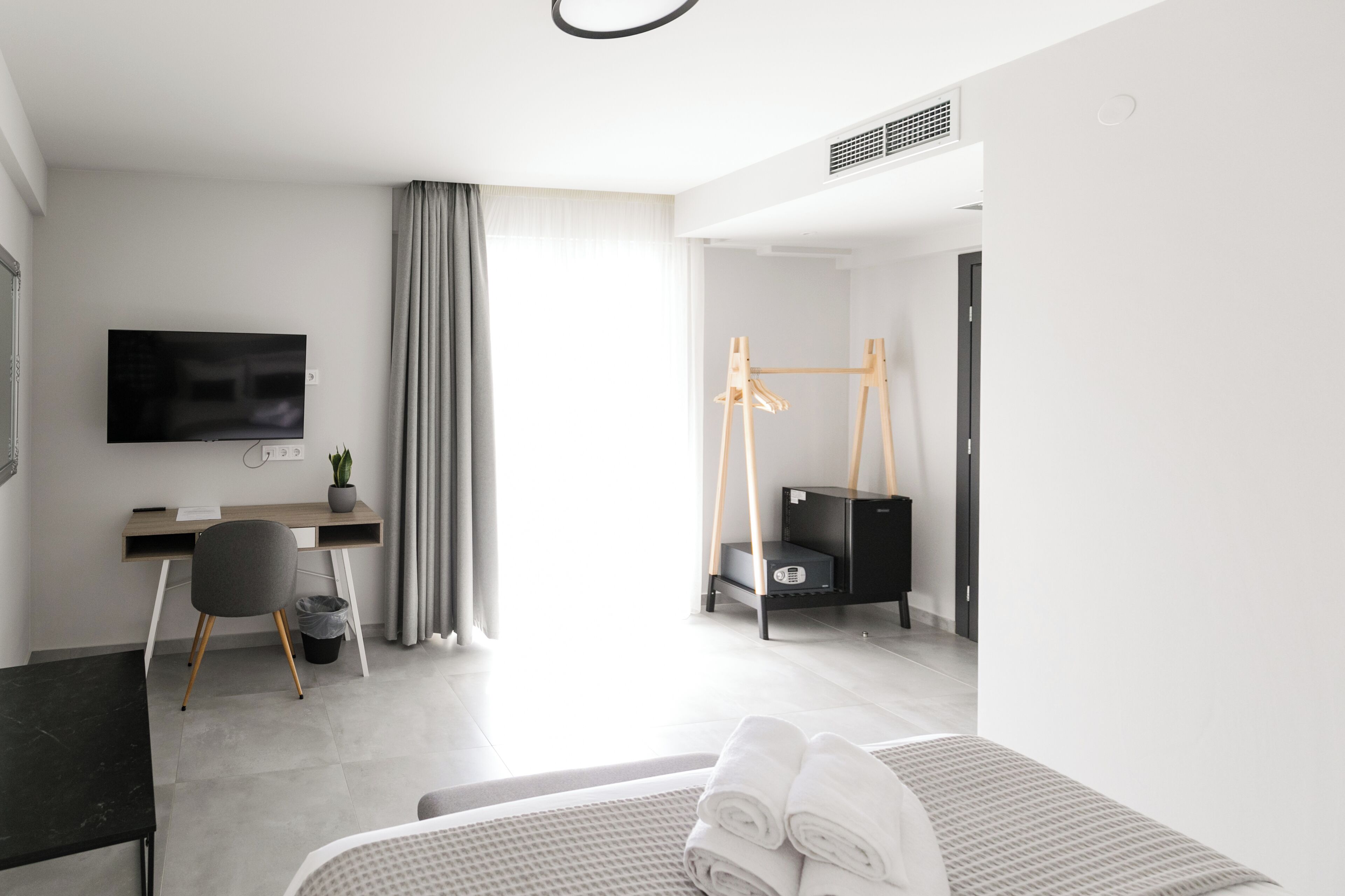 Una habitación de hotel moderna con cama, escritorio, silla, televisión y una planta pequeña.