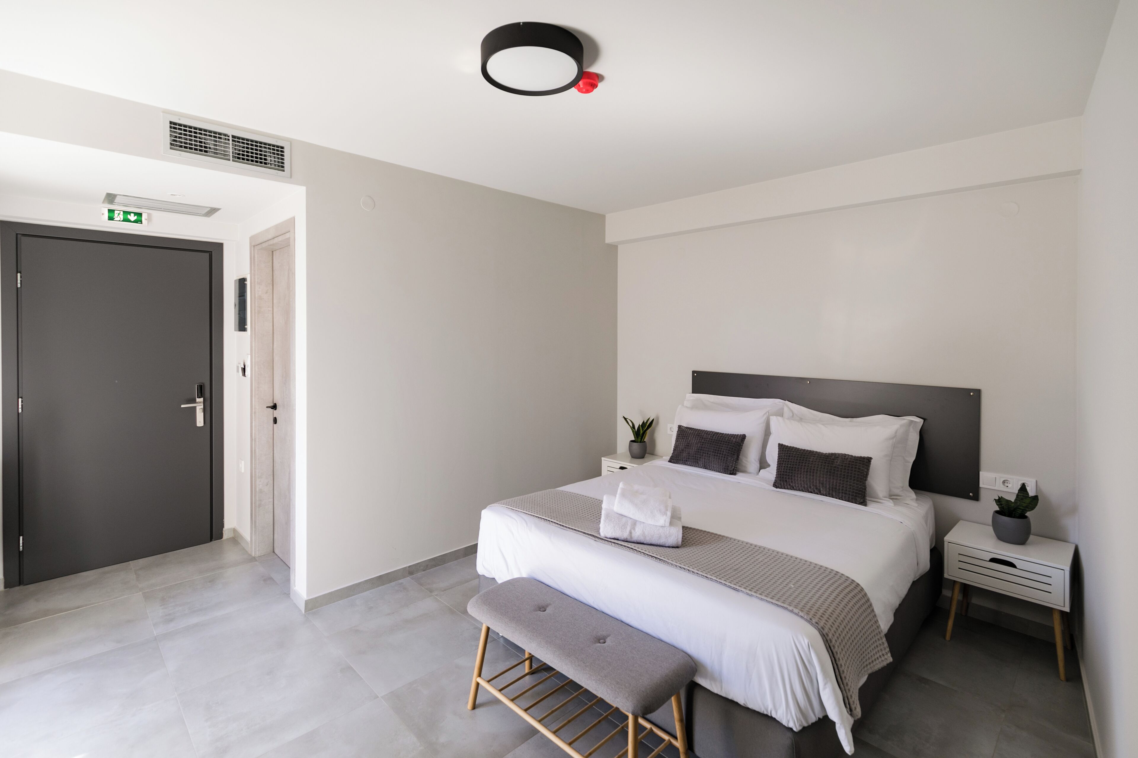 Un dormitorio moderno con una cama grande, mesitas de noche, un banco y una puerta.