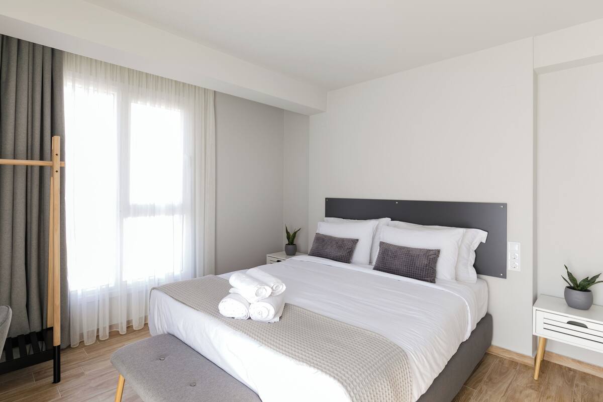 Een moderne hotelkamer met een groot bed, een nachtkastje met een plant en een raam met gordijnen.