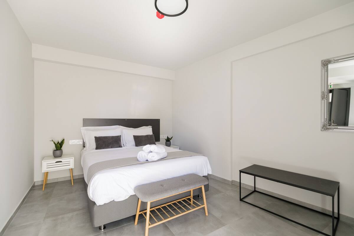 Een moderne slaapkamer met een bed, nachtkastjes, een bankje en een spiegel.