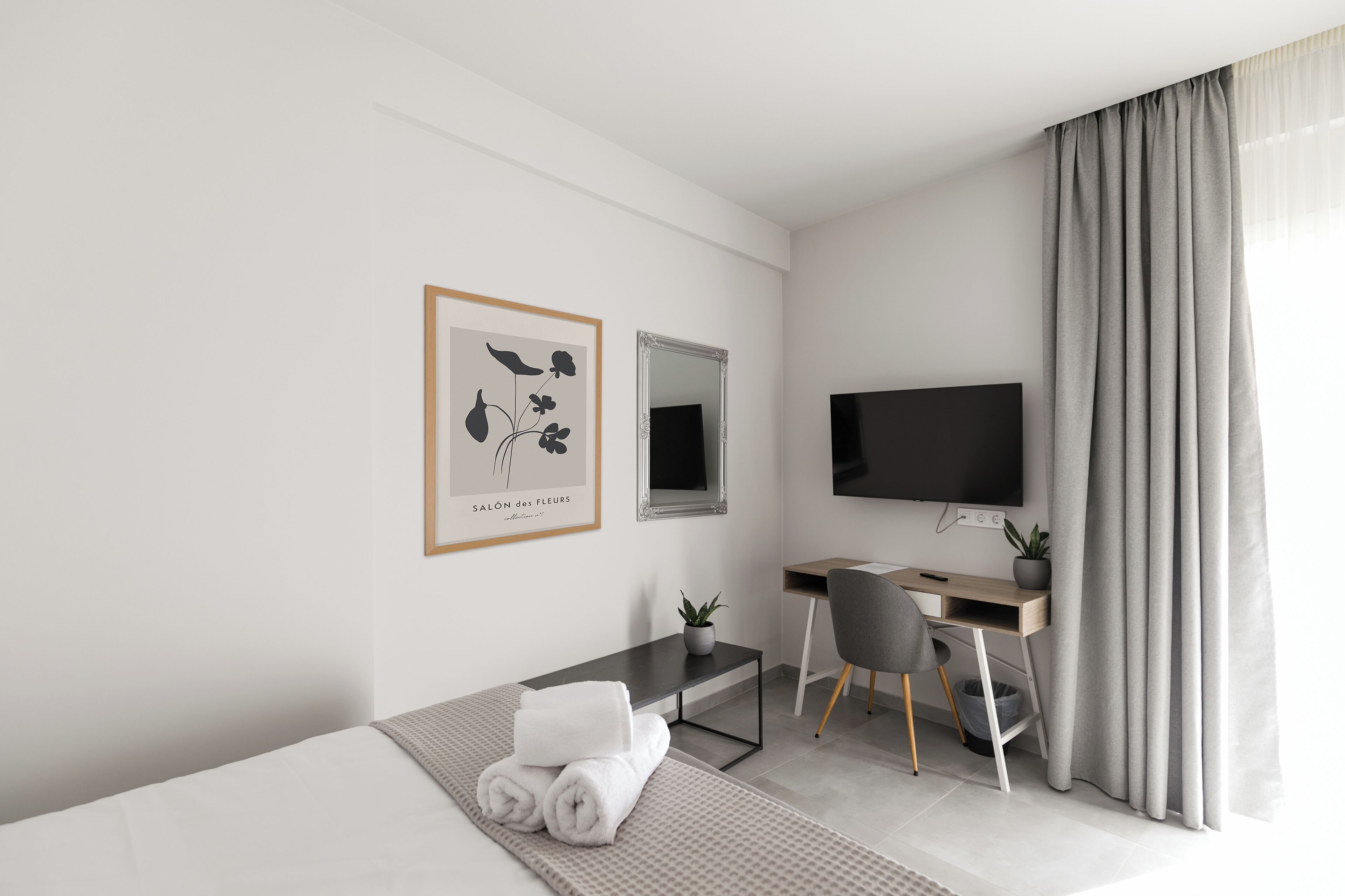 A modern hotel room with a bed, a desk, a chair, a television, and a framed artwork on the wall.