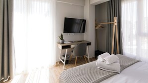 Ein modernes Hotelzimmer mit einem Bett, einem Schreibtisch, einem Fernseher und einem Vorhangfenster.