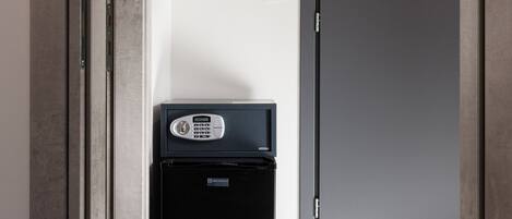 Un pasillo con una puerta, un letrero de salida de emergencia en la pared y un pequeño dispositivo negro fijado a la pared.