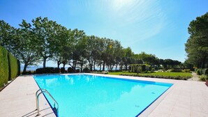 Une piscine rectangulaire, bordée d’une terrasse carrelée et entourée de haies et d’arbres soigneusement taillés.