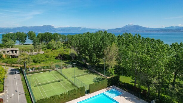 Un court de tennis avec une piscine, entouré d’arbres, et offrant une vue sur les montagnes et un lac.
