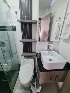 Un baño moderno con inodoro, lavamanos y cabina de ducha de vidrio.