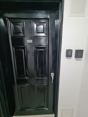 Una puerta negra con el número 403, un teclado numérico y un timbre en una pared blanca.