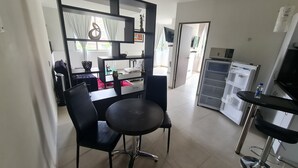 Un espace repas moderne avec une table ronde et des chaises, un téléviseur encadré de noir et un réfrigérateur.