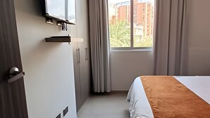 Une chambre d’hôtel avec un lit, un téléviseur fixé au mur, une fenêtre avec des rideaux et une porte.