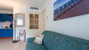 Uma sala de estar com um sofá azul-turquesa, uma poltrona com almofada, um abajur e um quadro na parede.