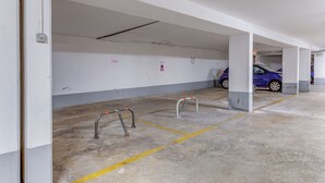Uma garagem de estacionamento vazia com piso de concreto, paredes brancas e um carro azul estacionado ao longe.