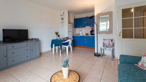 Uma sala de estar moderna com televisão, armários cinza, uma mesa de jantar com cadeiras e um sofá azul.