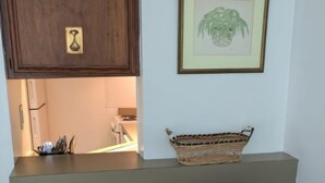 Un salon avec un fauteuil à rayures, un meuble en bois, une étagère sur laquelle se trouve un panier en osier, et un tableau encadré accroché au mur.