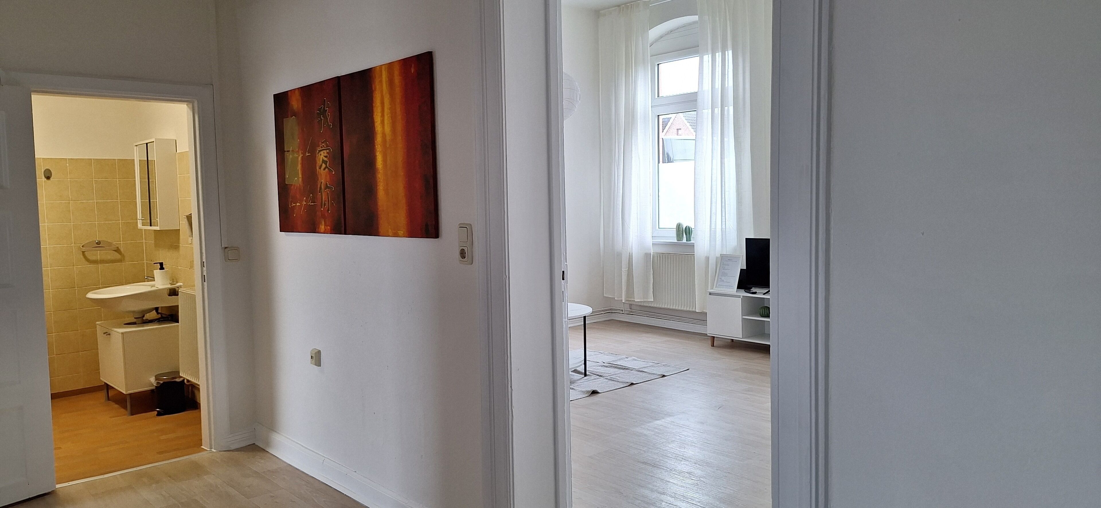 A hallway leading to a bathroom with a sink, mirror, and towel rack. A painting is visible on the wall.