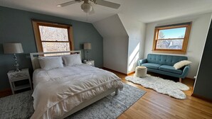 Un dormitorio con cama, dos mesitas de noche, un sofá azul, una alfombra blanca y un ventilador de techo.