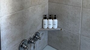 Zona de ducha con cabezal de ducha manual, estante empotrado con tres botellas y diseño de azulejos en esquina.