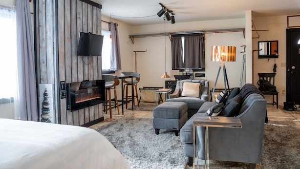 A modern hotel room with a bed, a sofa, a TV, a fireplace, and a dining area. - Orchard Apartment @ The Copper Crown, Bayfield (Bayfield)